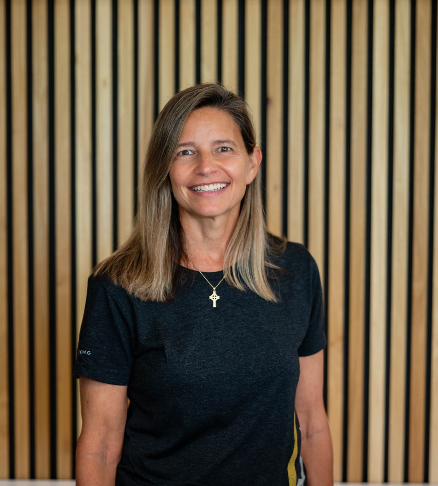 Smiling woman standing against wooden slat background.