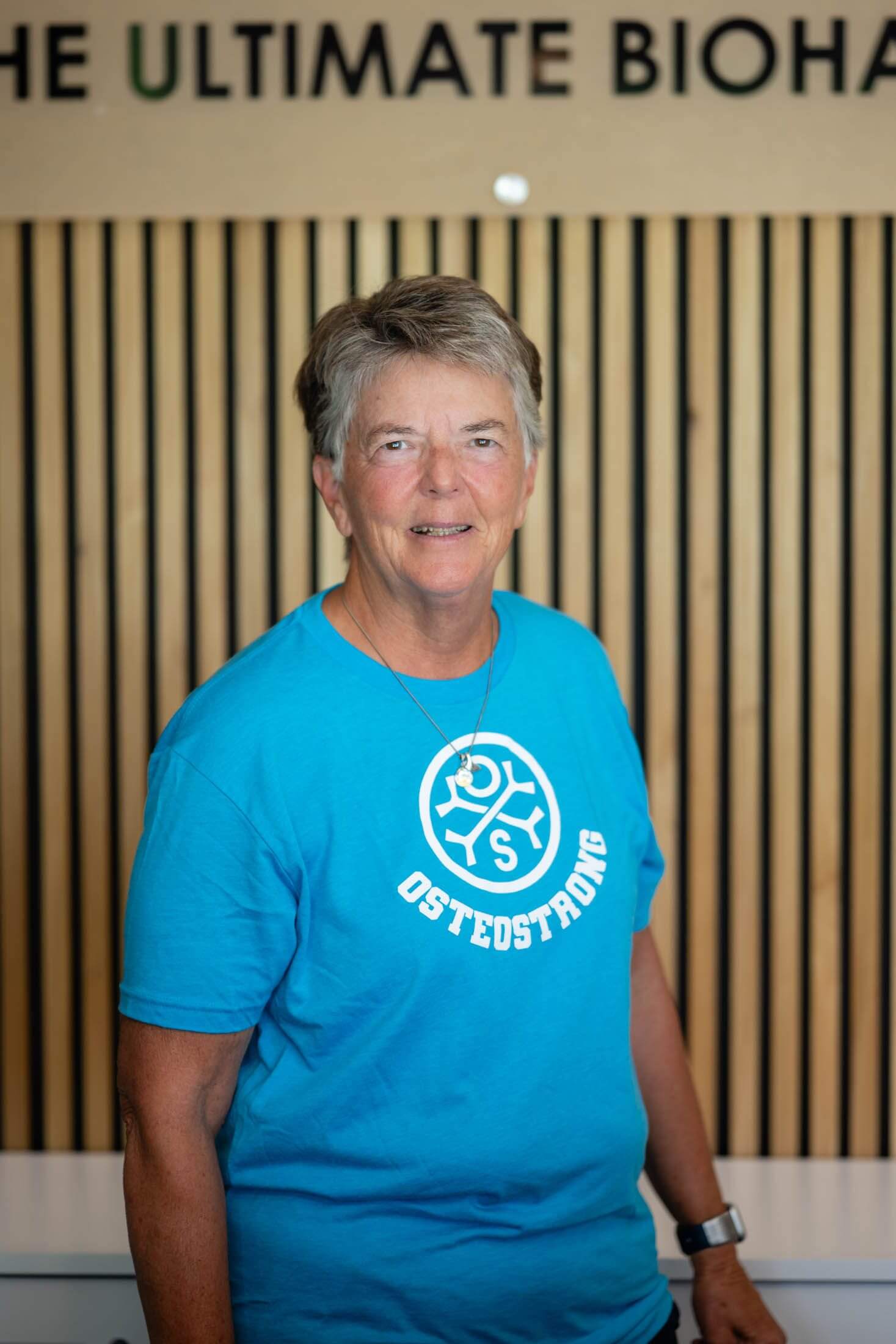 Person wearing blue "Osteostrong" t-shirt, smiling.